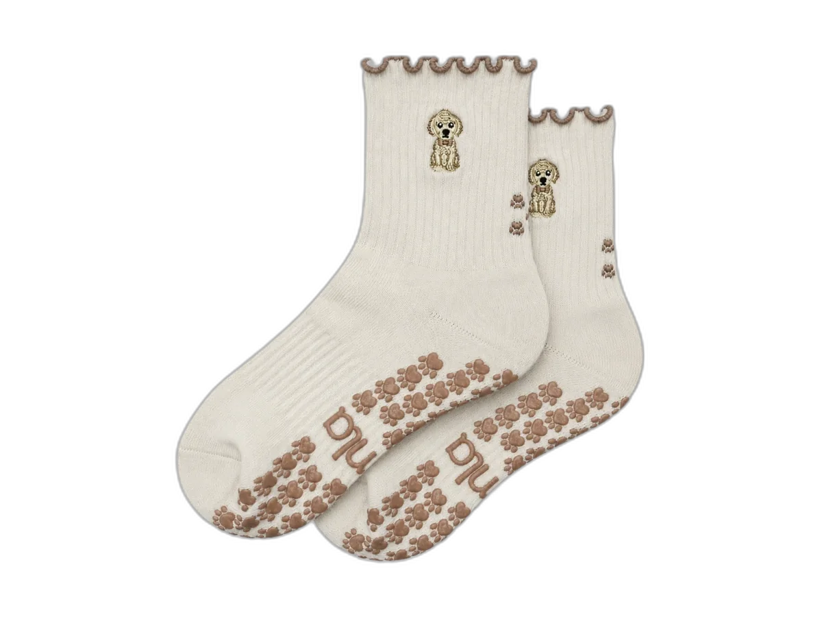 Pair of cream Almla Golden Retriever Pilates grip socks with brown paw-print sole grips on a transparent background