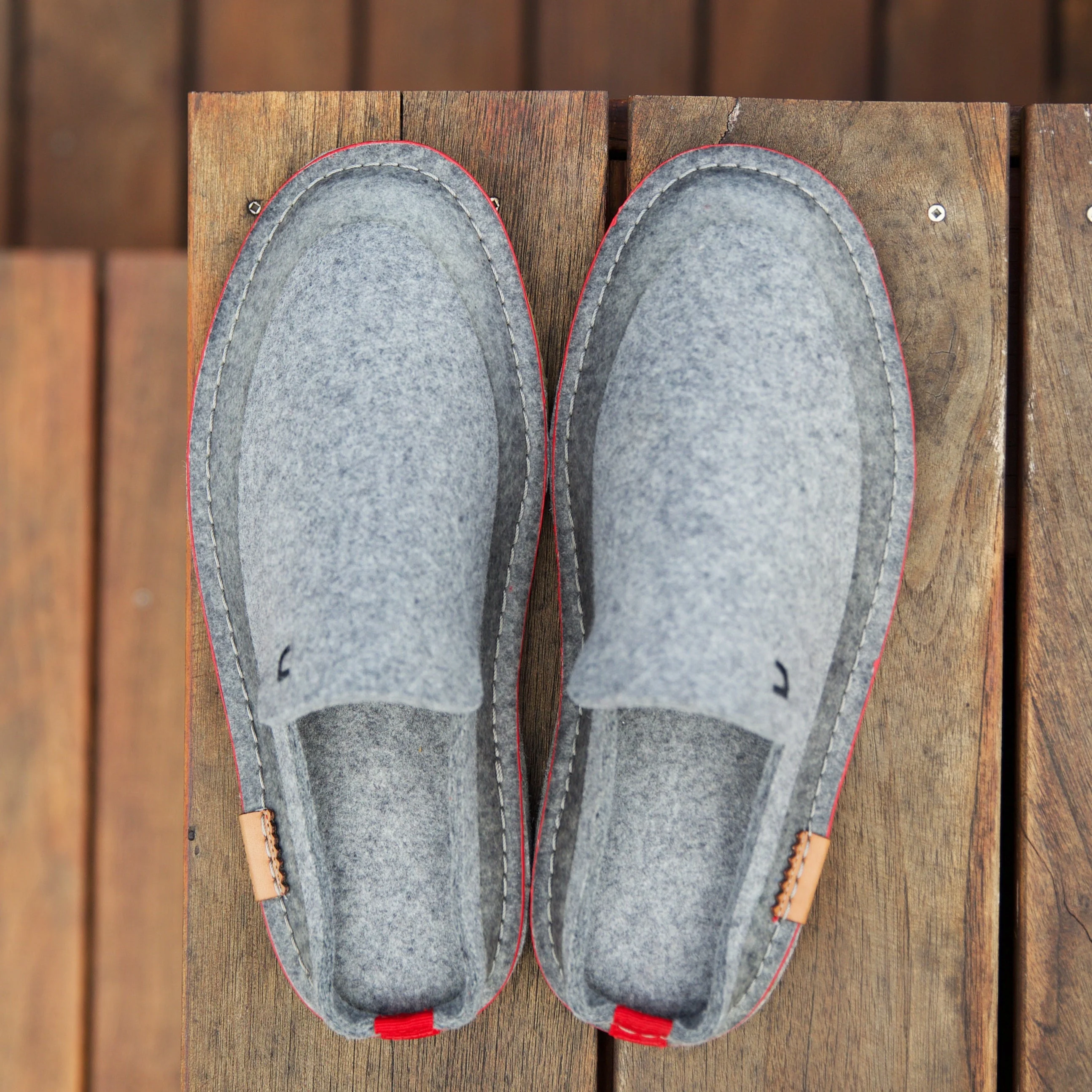 Pair of Canoe Footwear The Wool Mule slippers shown on a natural wood surface.