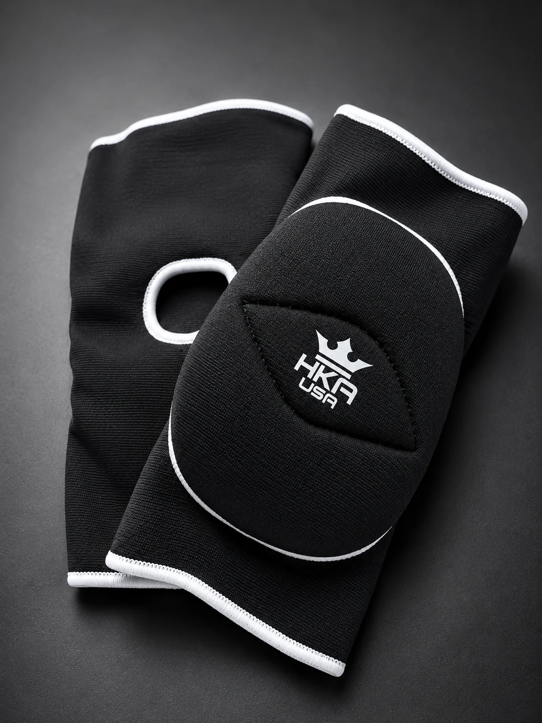 Black HKA USA knee pads with raised kneecap padding and white trim on a gray studio background.