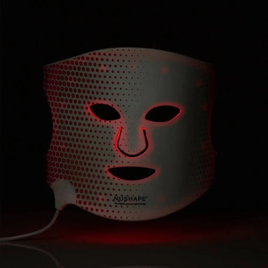 White NuShape LED face mask with red lights illuminated against a dark background.